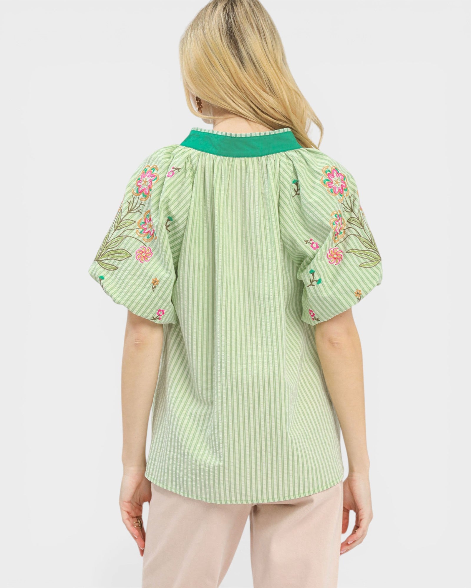 Person wearing a green blouse with floral embroidery on a white background