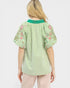 Person wearing a green blouse with floral embroidery on a white background