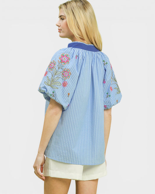 Woman wearing a light blue blouse with floral embroidery on a white background