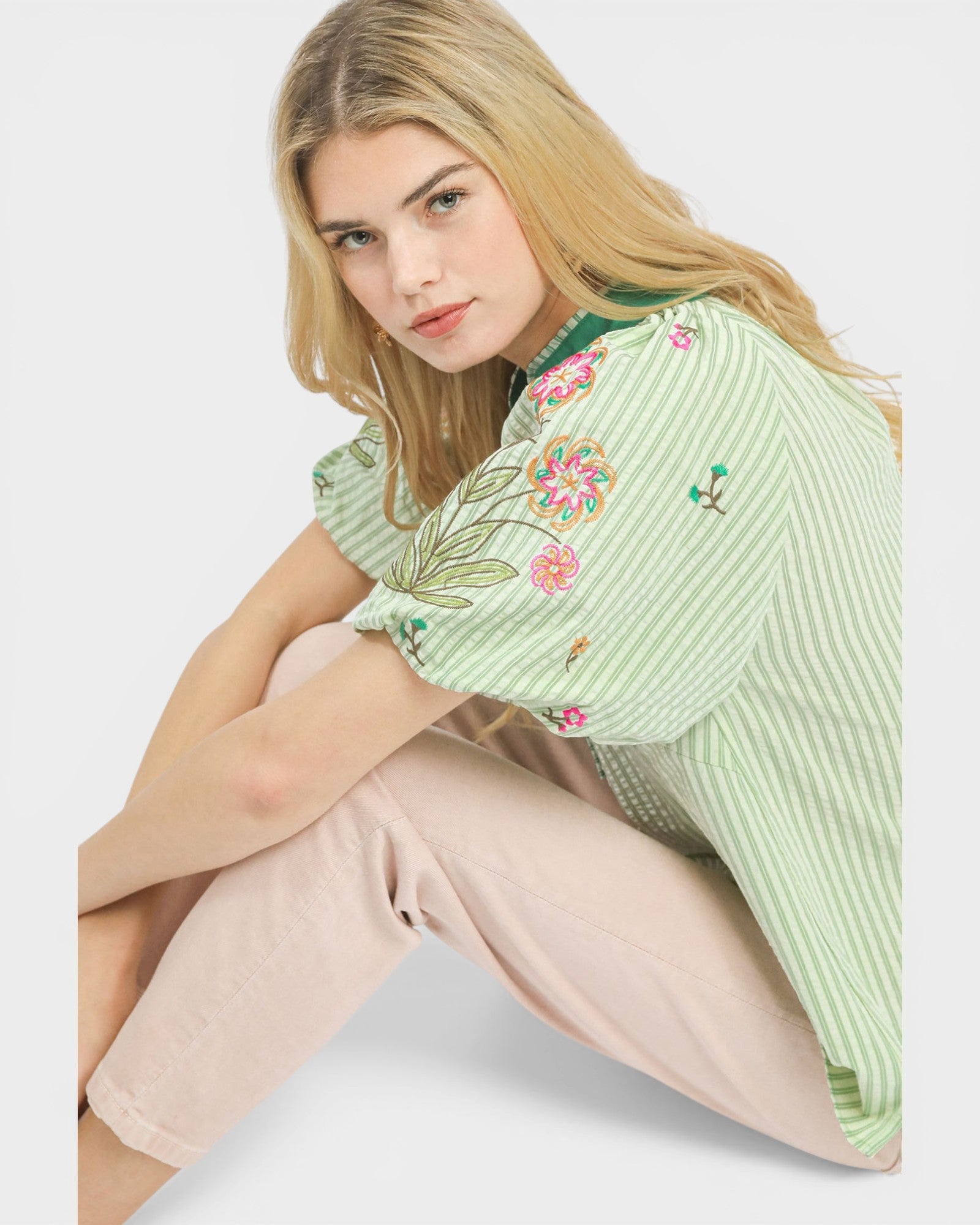 Woman wearing a green embroidered blouse sitting on a white surface