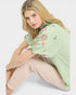 Woman wearing a green embroidered blouse sitting on a white surface
