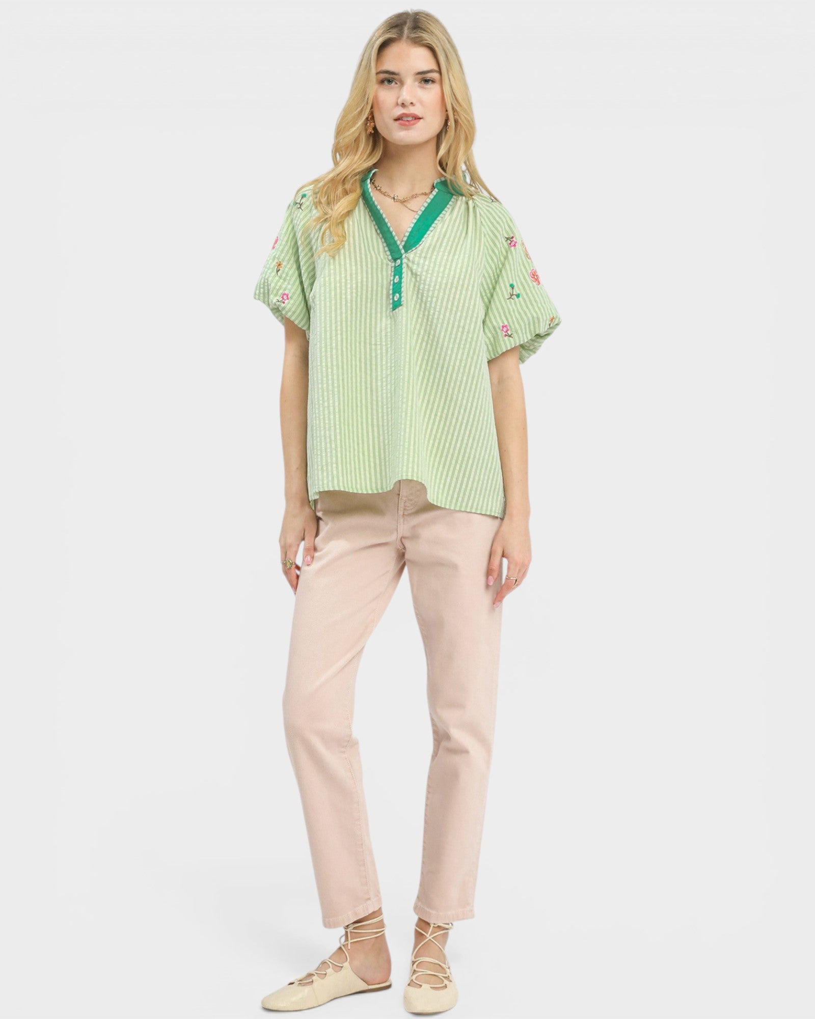 Woman wearing a green checkered blouse with floral embroidery and light pink pants on a white background
