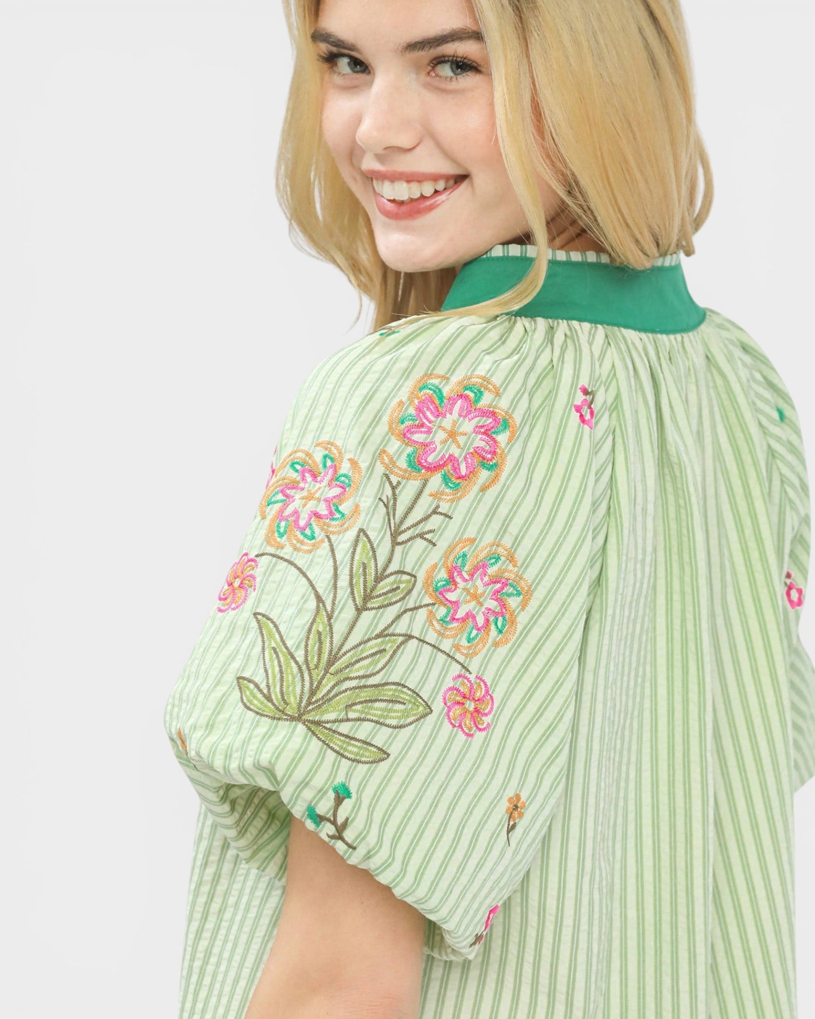 Woman wearing a green embroidered dress with floral patterns on a white background
