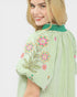 Woman wearing a green embroidered dress with floral patterns on a white background