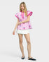Woman wearing a pink embroidered top and white shorts on a light gray background