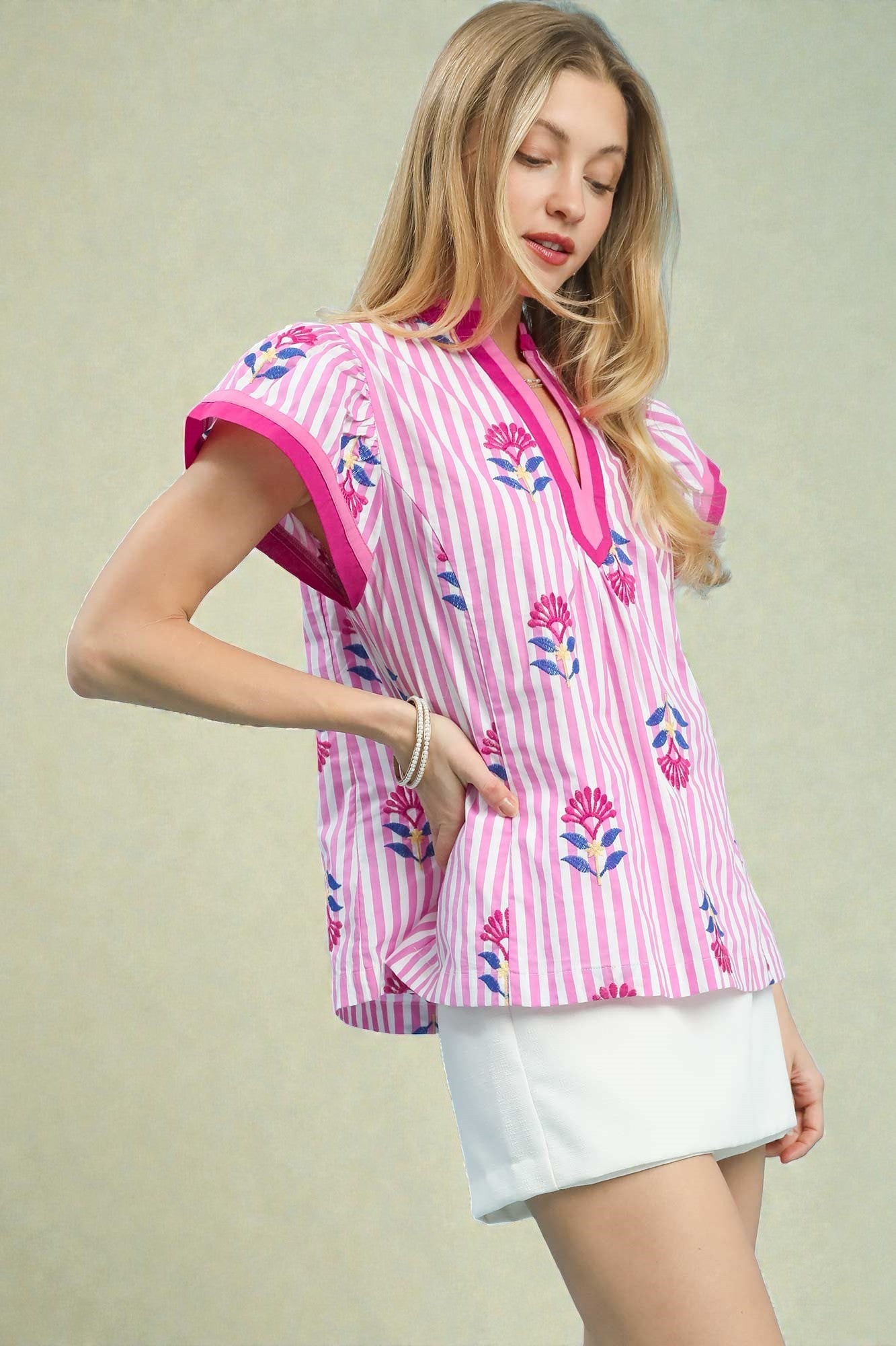 Woman wearing a pink and white striped blouse with floral patterns on a plain background
