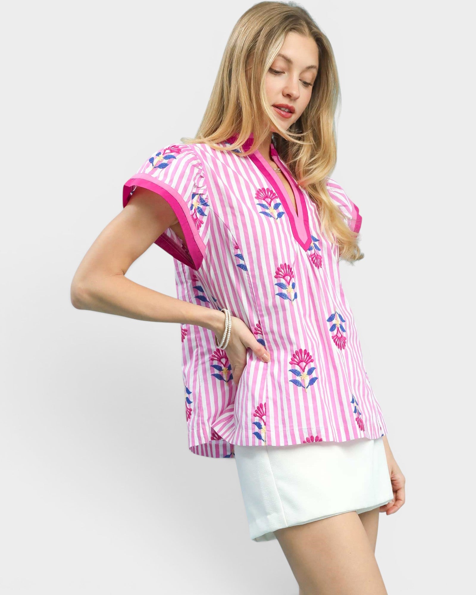 Woman wearing a pink and white striped shirt with floral patterns on a plain background