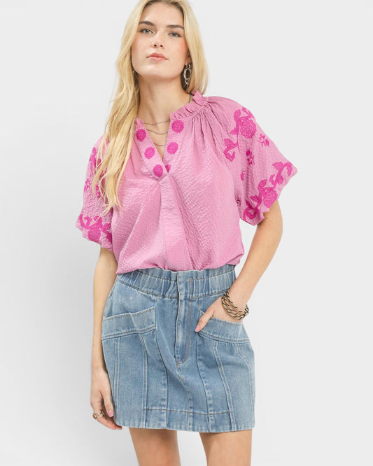 Woman wearing a pink blouse with floral embroidery and a denim skirt on a white background