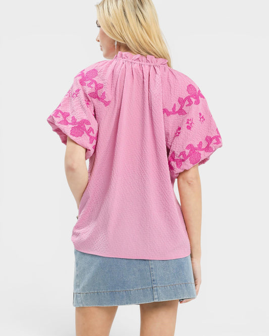 Person wearing a pink blouse with floral patterns on a white background