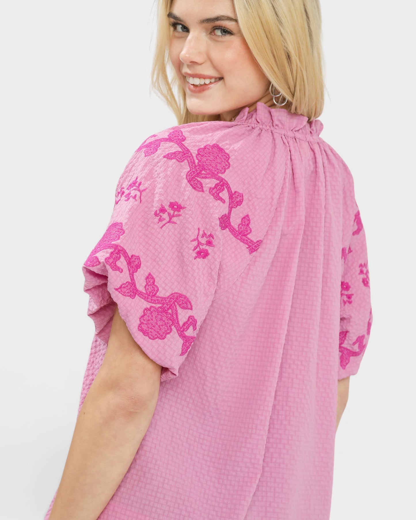 Woman wearing a pink dress with floral embroidery on a white background