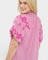 Woman wearing a pink dress with floral embroidery on a white background