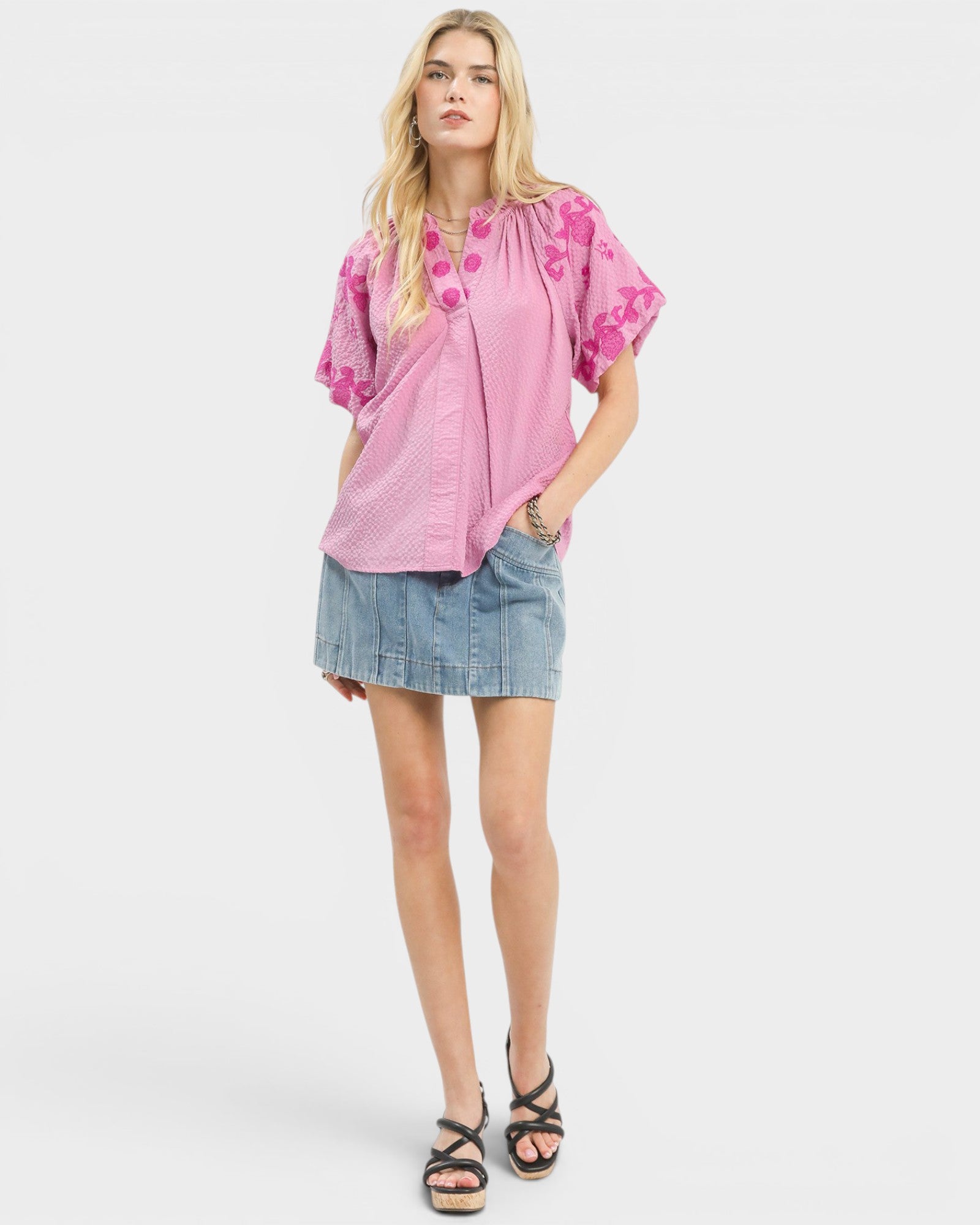 Woman wearing a pink blouse with floral patterns and a denim skirt on a white background