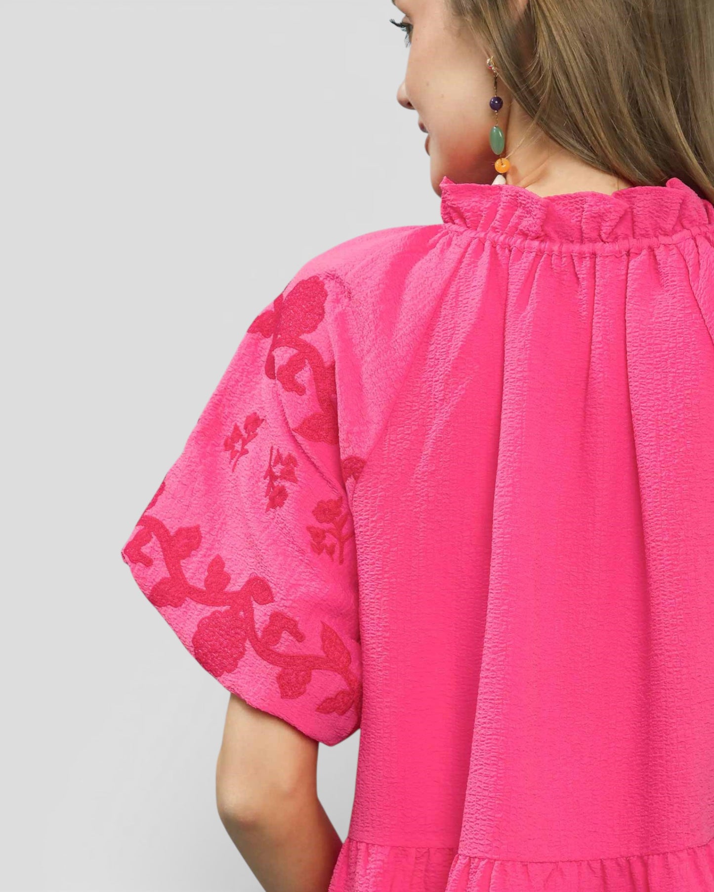 Pink blouse with floral embroidery on sleeves against a gray background
