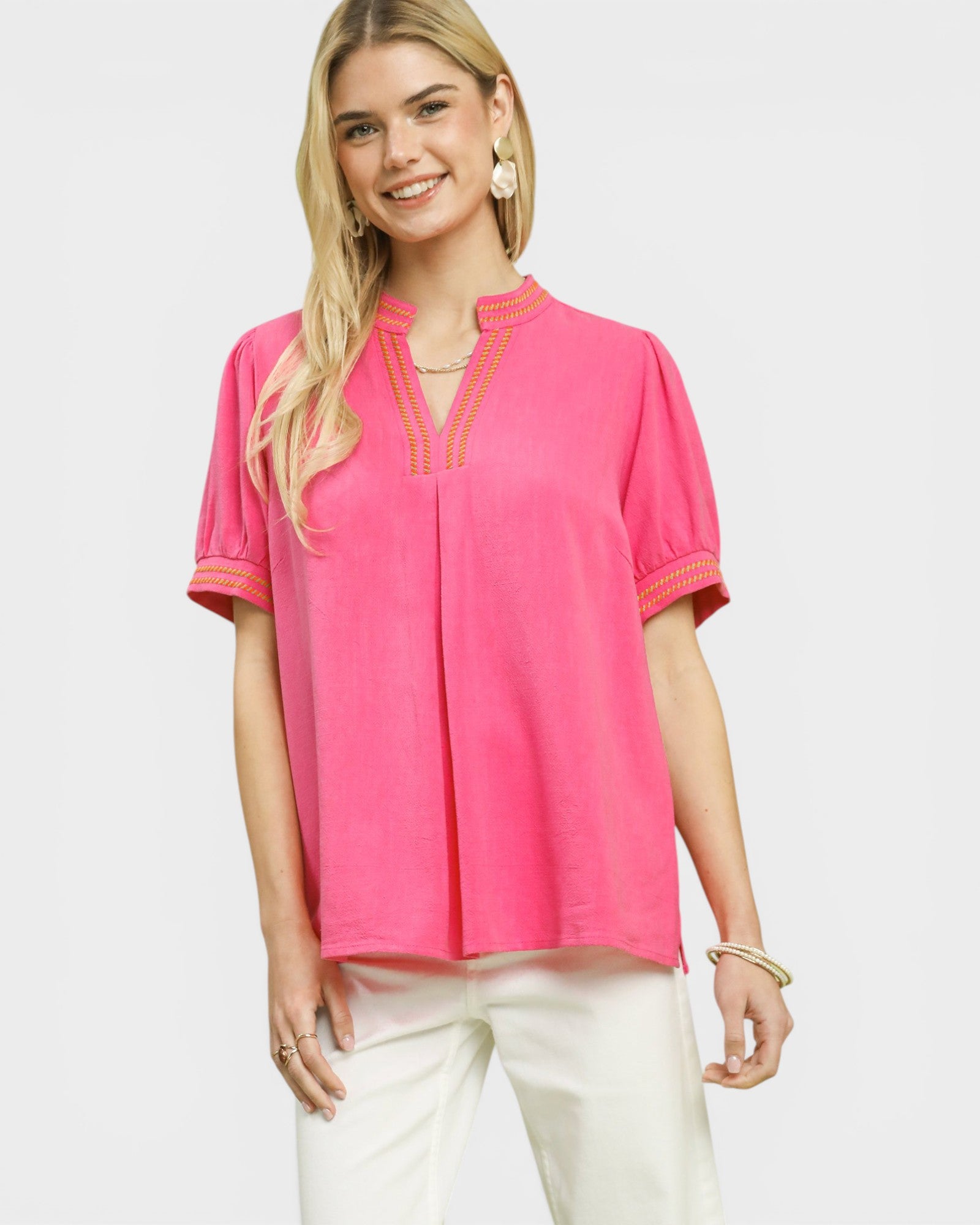 Woman wearing a pink blouse with white pants on a light gray background