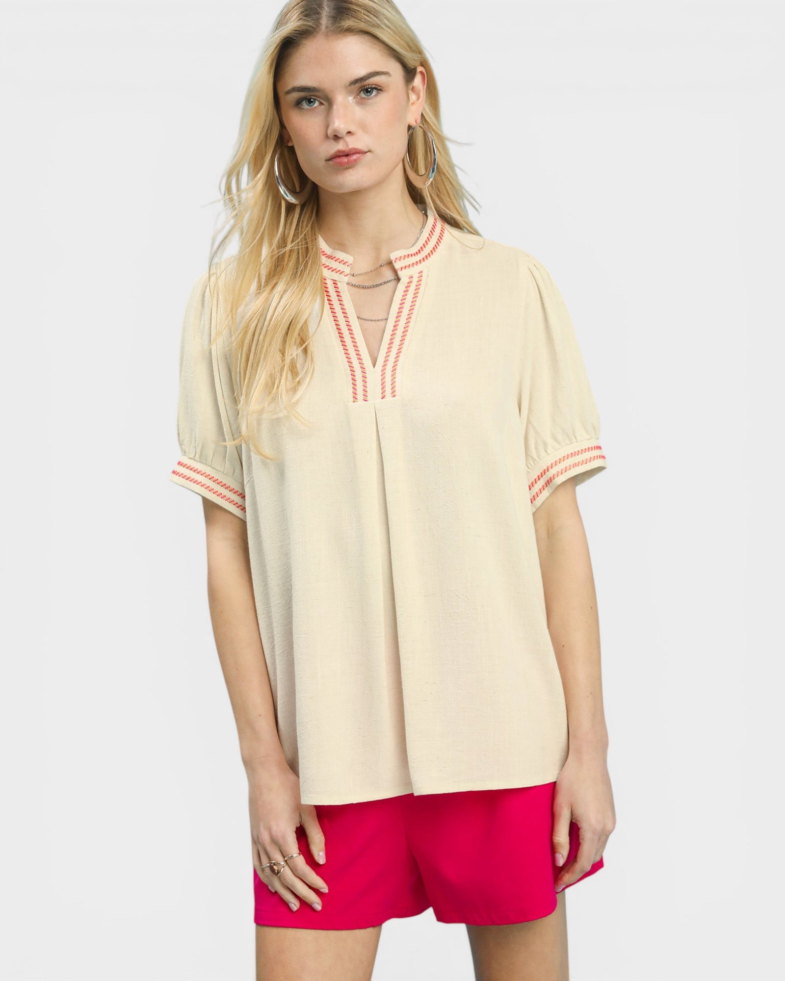 Woman wearing a beige blouse with red accents and pink shorts on a white background