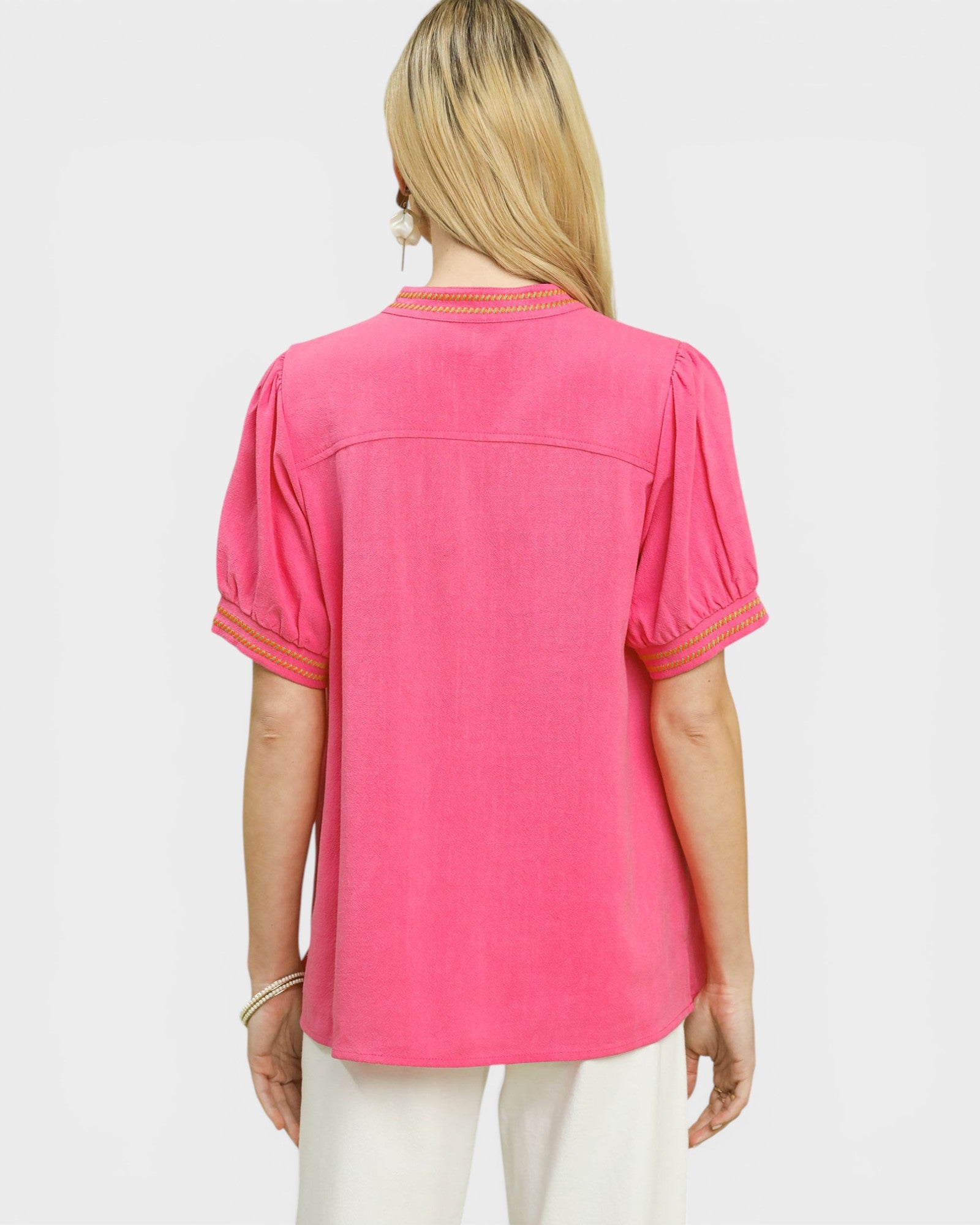 Woman wearing a pink blouse with white pants on a light gray background