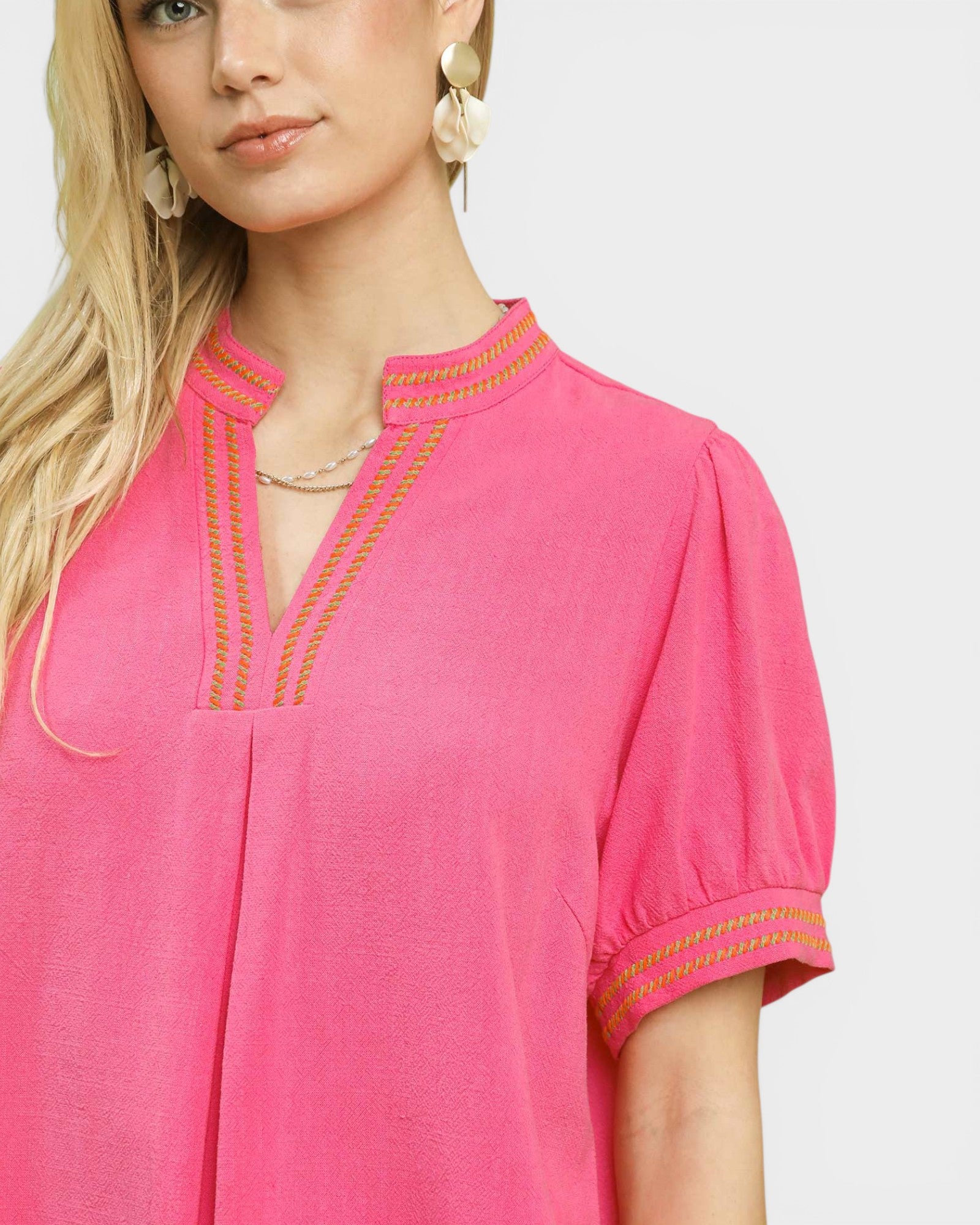 Close-up of a pink top with gold embroidery on a plain background