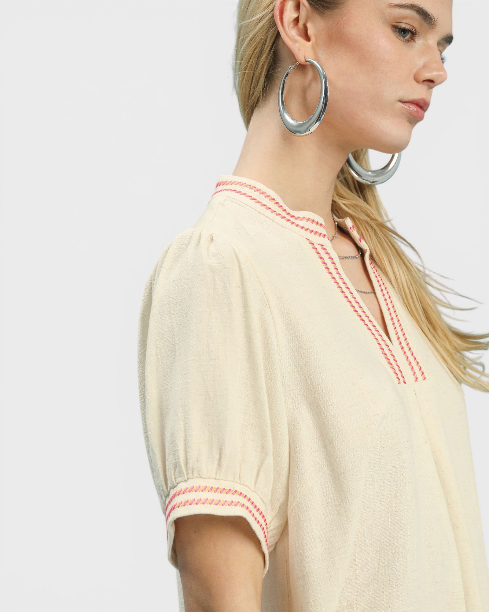 Woman wearing a beige blouse with red stitching on a white background