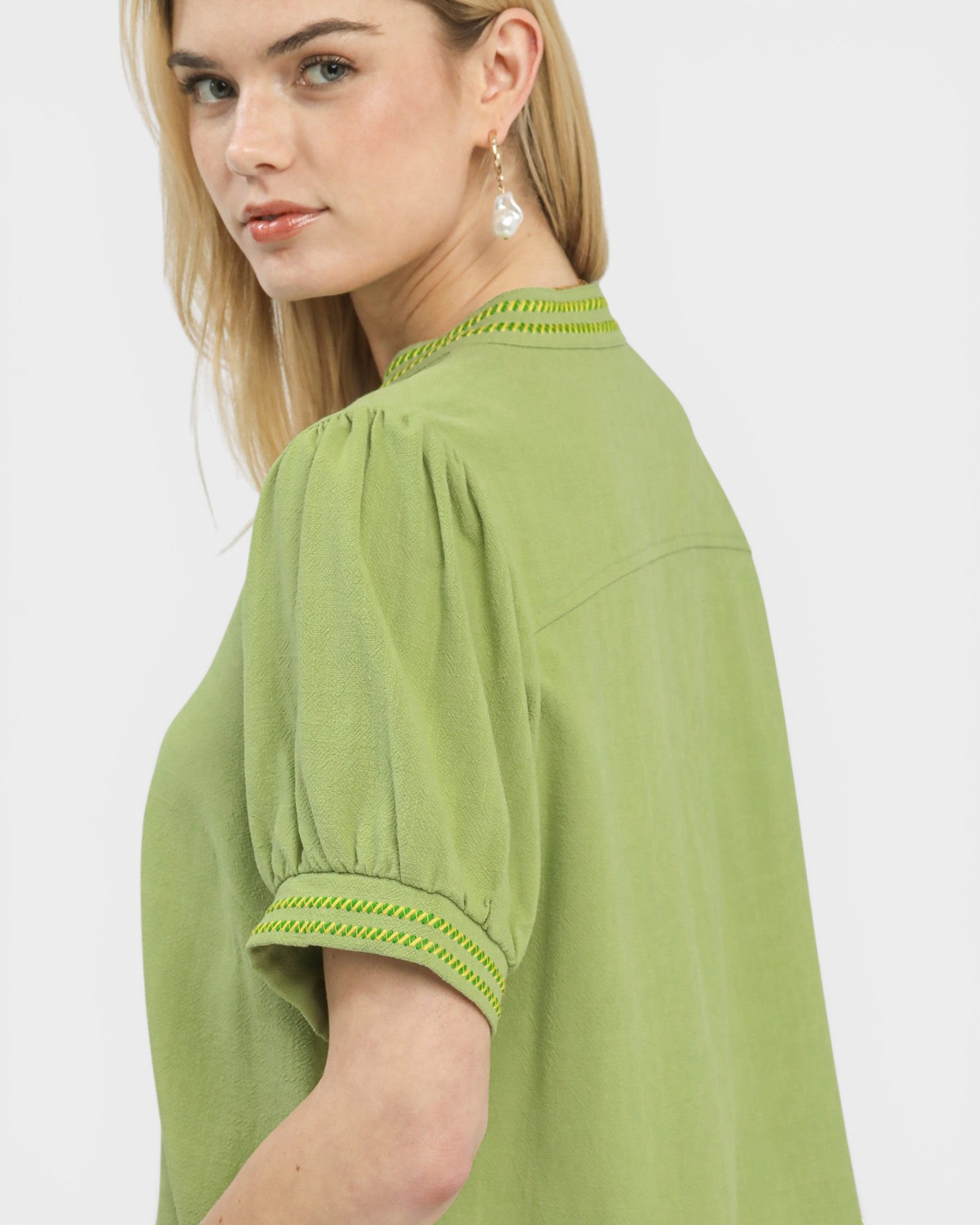 Woman wearing a green blouse with embroidered details on a white background
