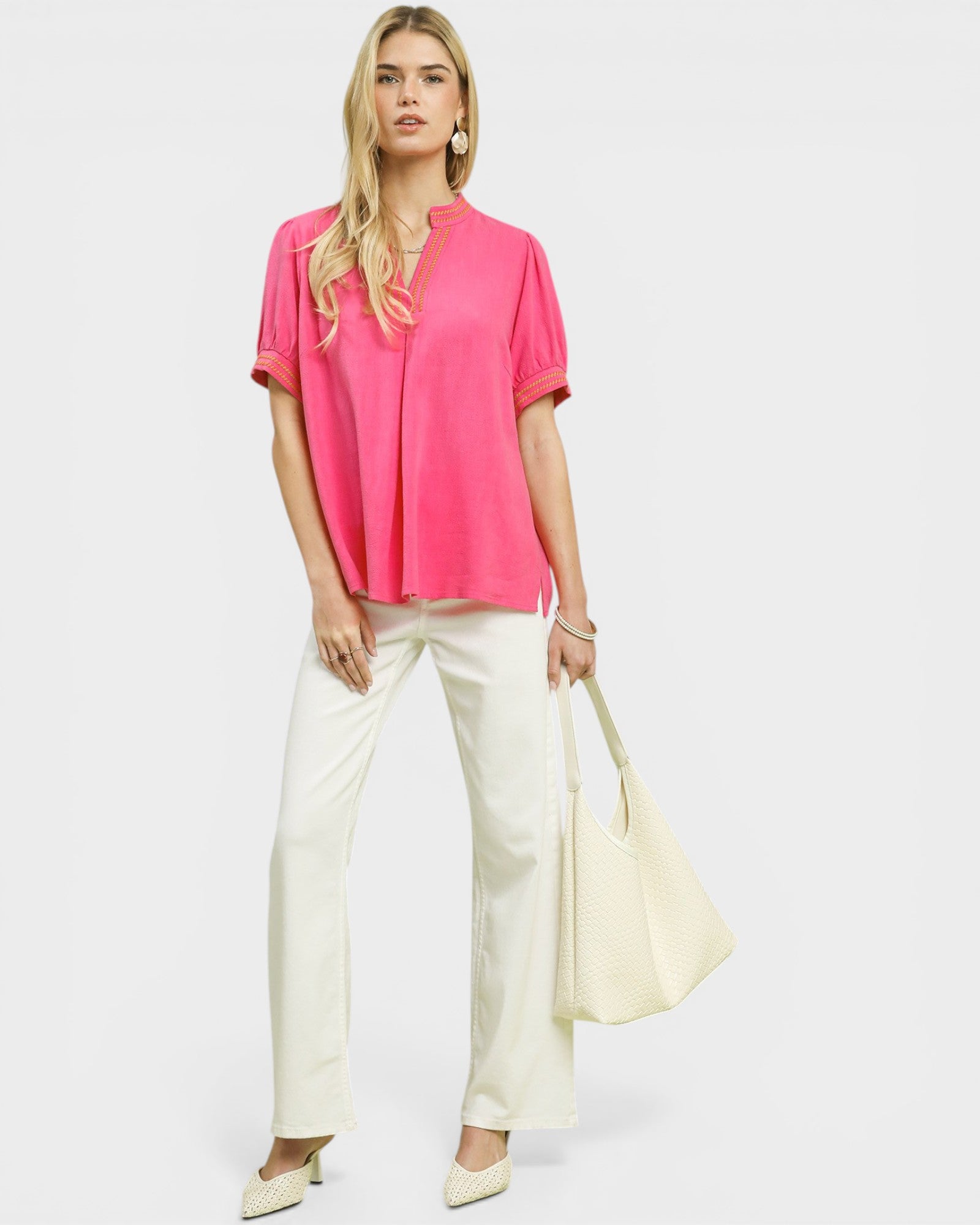 Woman wearing a bright pink top and white pants on a plain background