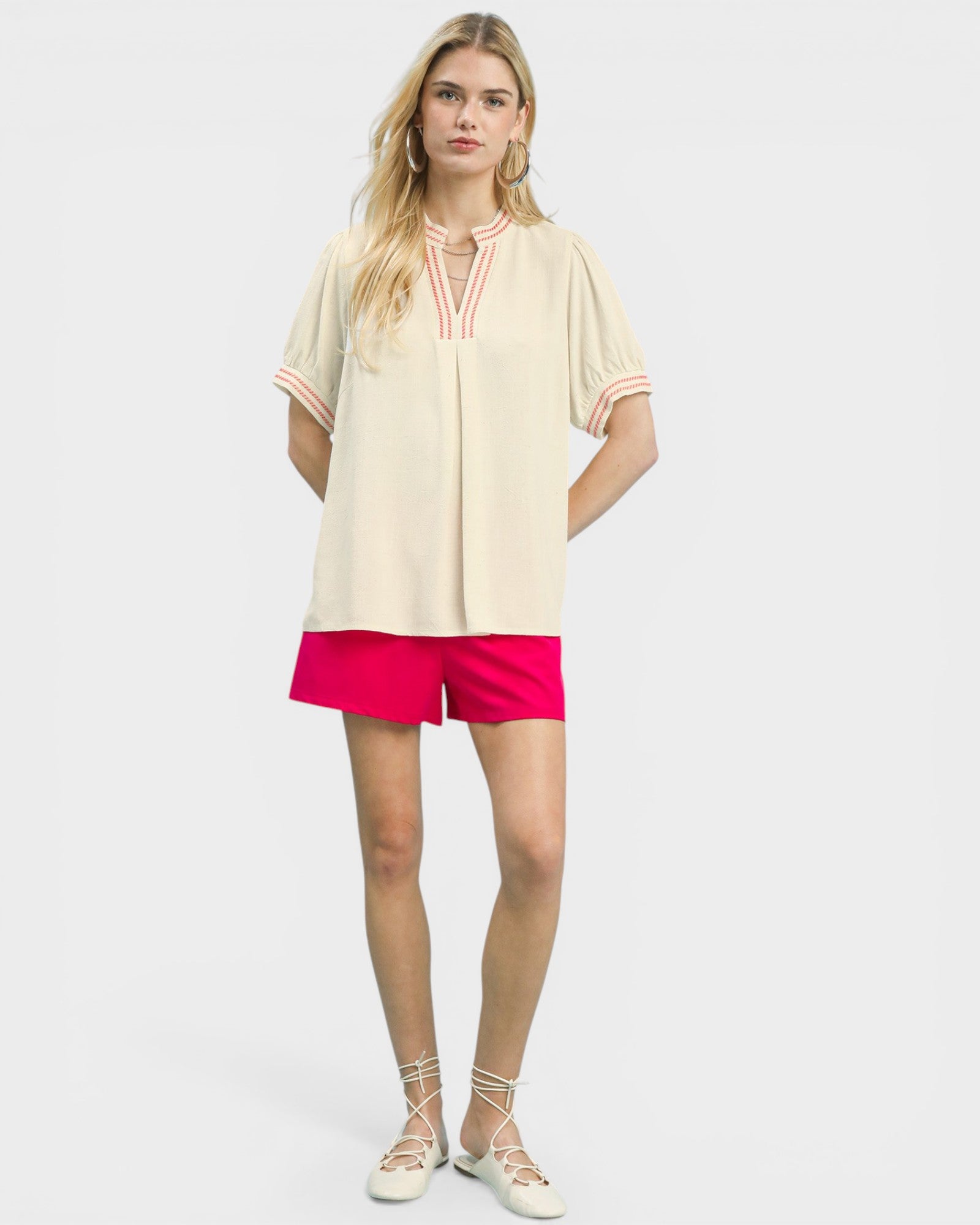 Woman wearing a beige top and pink shorts on a white background
