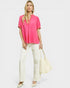 Woman wearing a bright pink top and white pants on a plain background