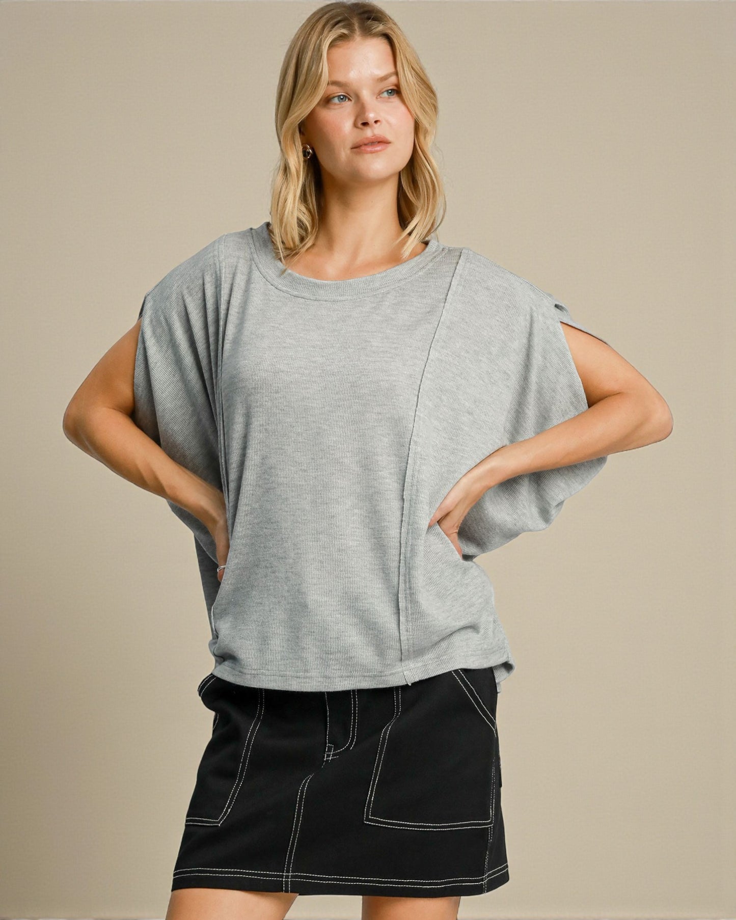 Woman wearing a gray oversized t-shirt and black skirt on a beige background