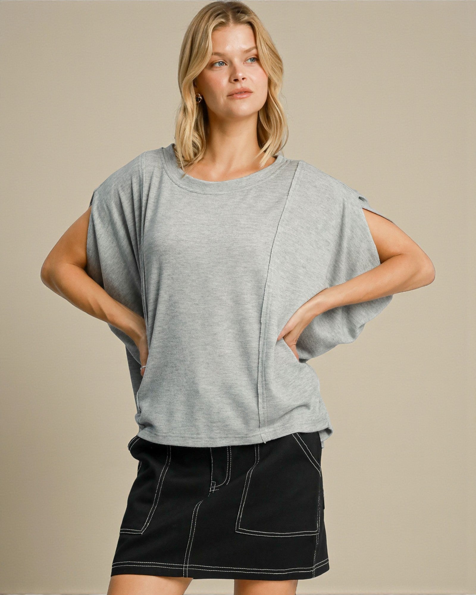 Woman wearing a gray oversized t-shirt and black skirt on a beige background