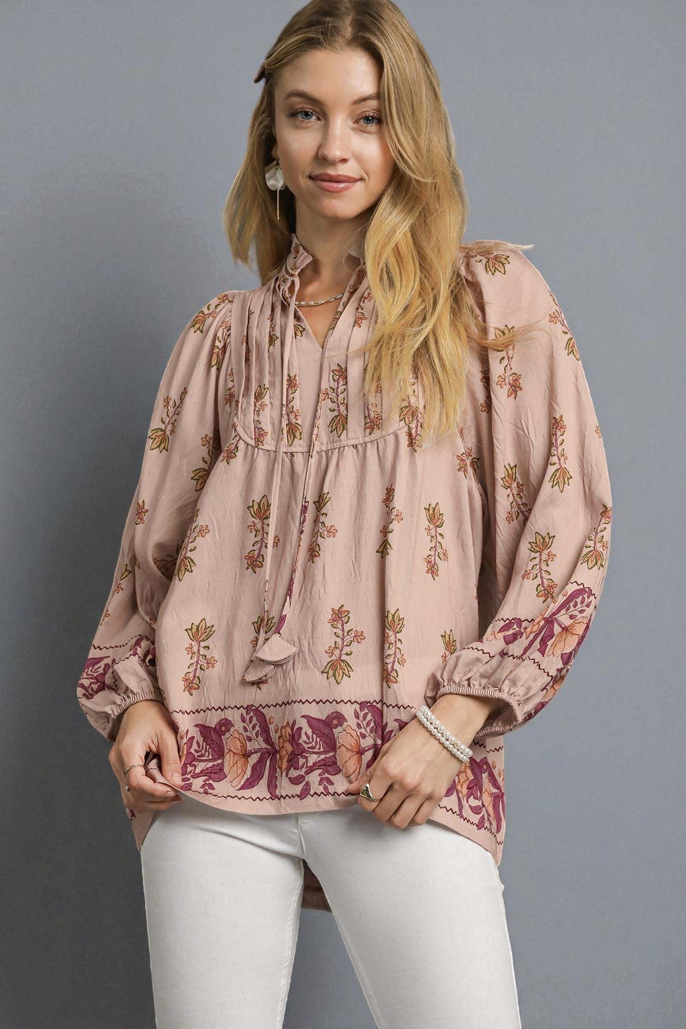 Woman wearing a floral blouse with long sleeves against a gray background