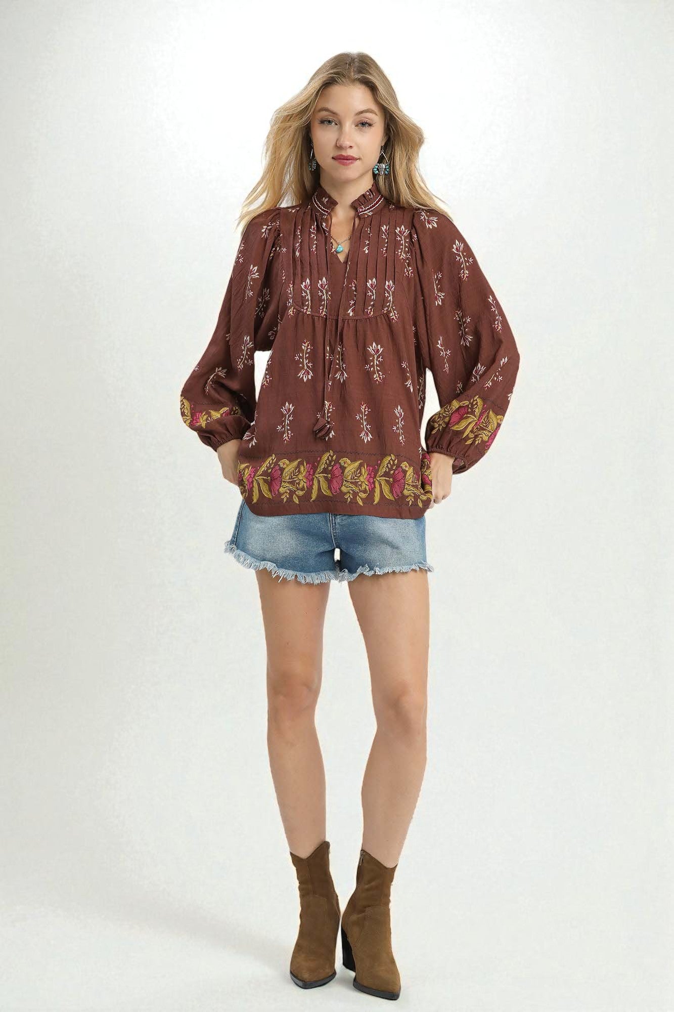 Woman wearing a patterned blouse, denim shorts, and brown boots on a white background