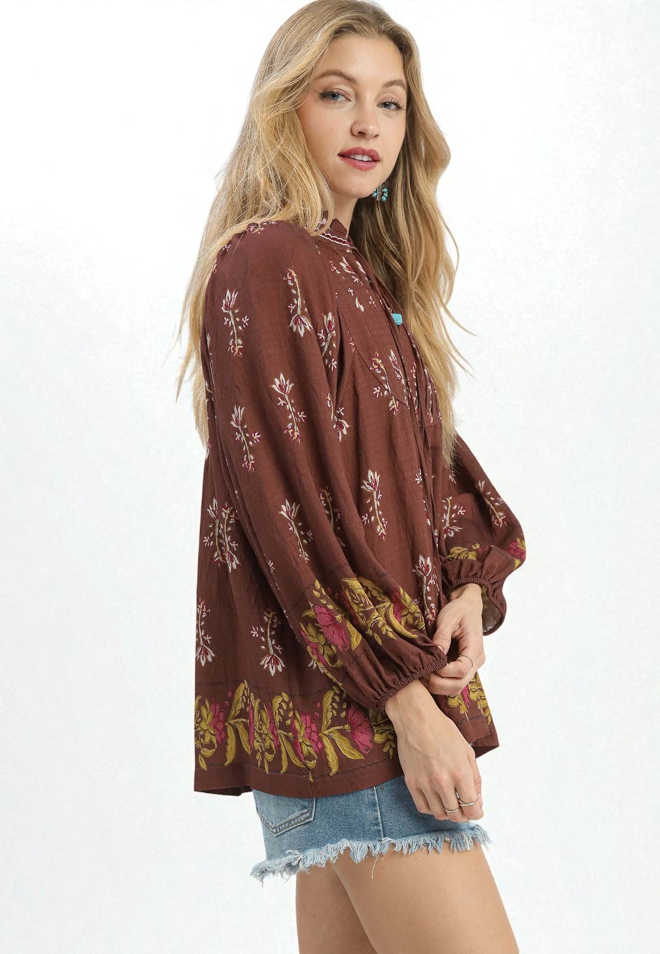 Woman wearing a brown floral blouse with denim shorts on a white background