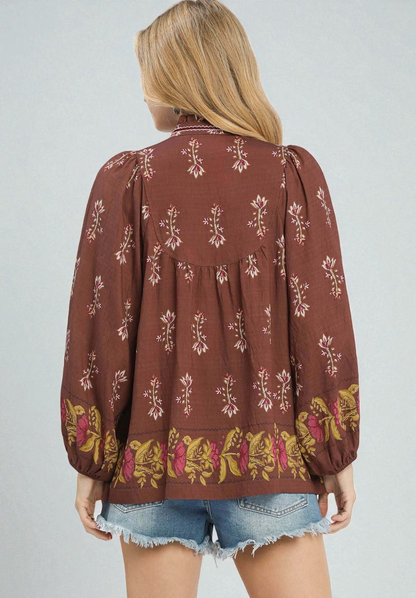 Woman wearing a brown patterned blouse with long sleeves on a plain background