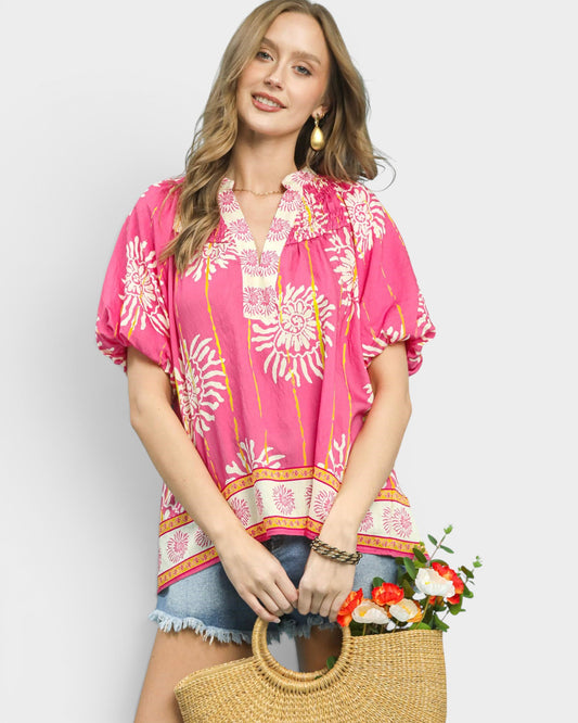 Woman wearing a pink floral blouse holding a straw bag with flowers against a white background