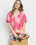 Woman wearing a pink floral blouse holding a straw bag with flowers against a white background
