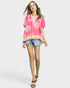 Woman wearing a pink floral blouse and denim shorts on a white background