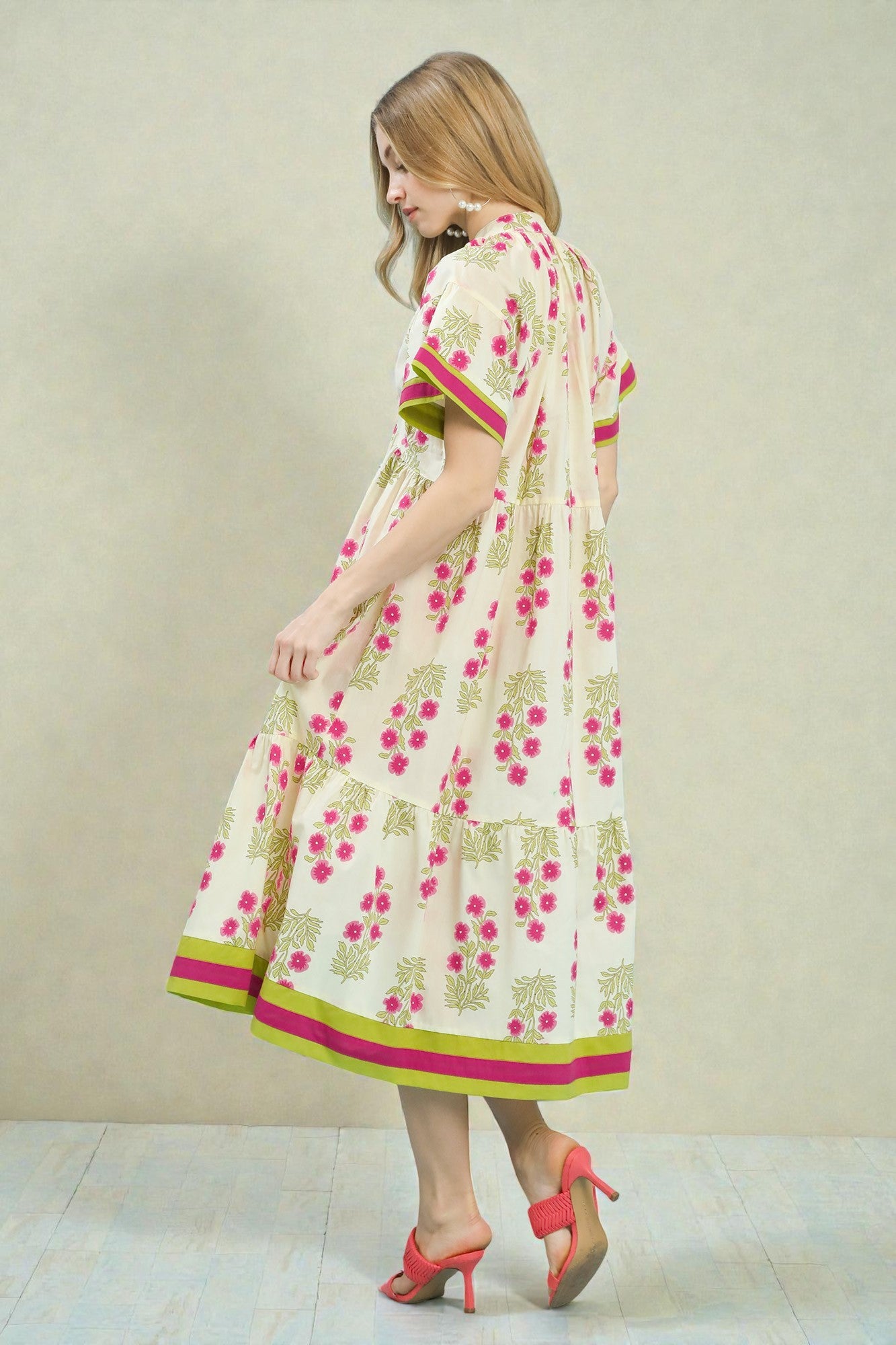 Woman wearing a floral dress with pink and green accents on a plain background