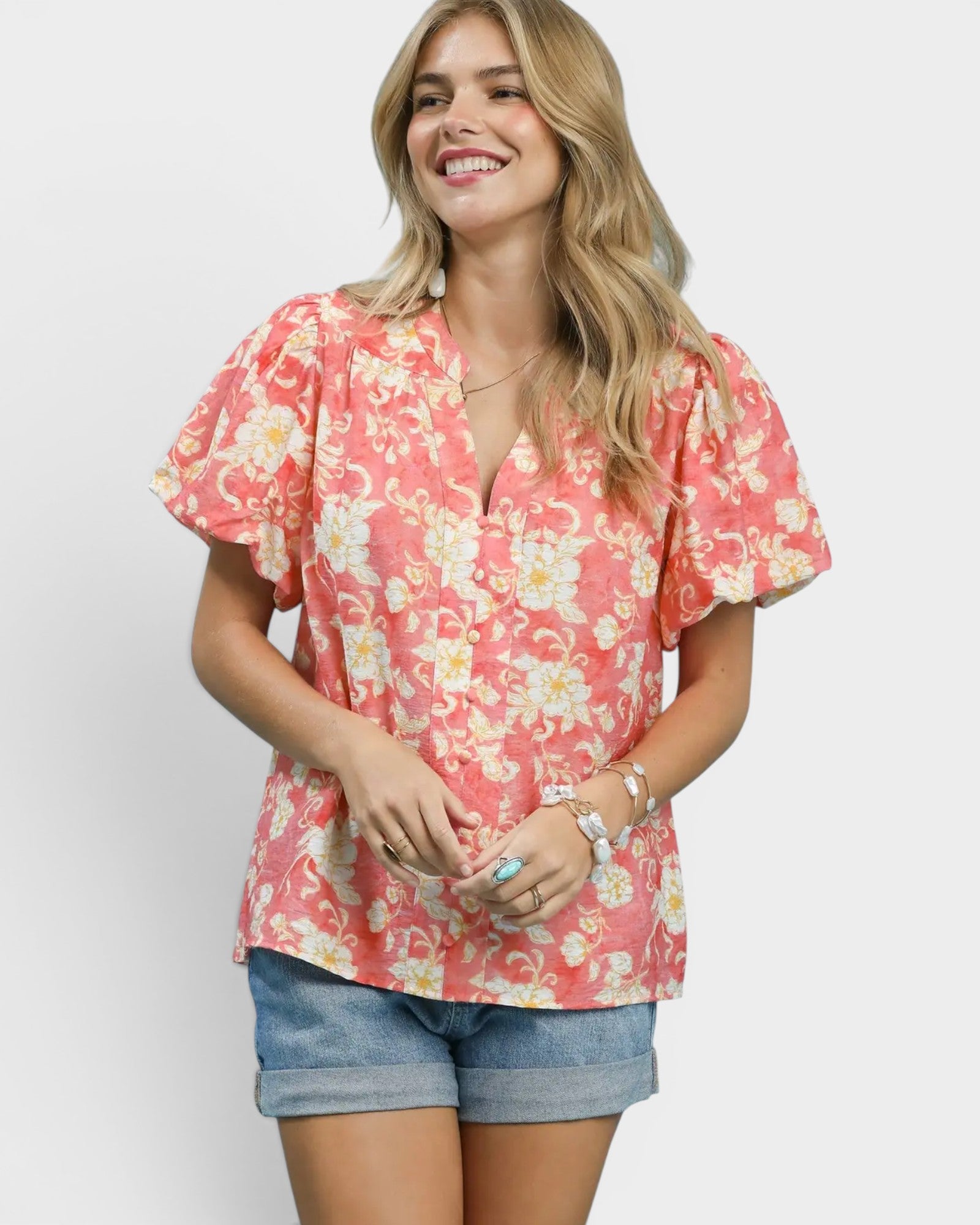 Woman wearing a pink floral blouse and denim shorts on a white background