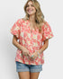 Woman wearing a pink floral blouse and denim shorts on a white background