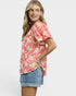 Woman wearing a pink floral blouse and denim shorts on a white background