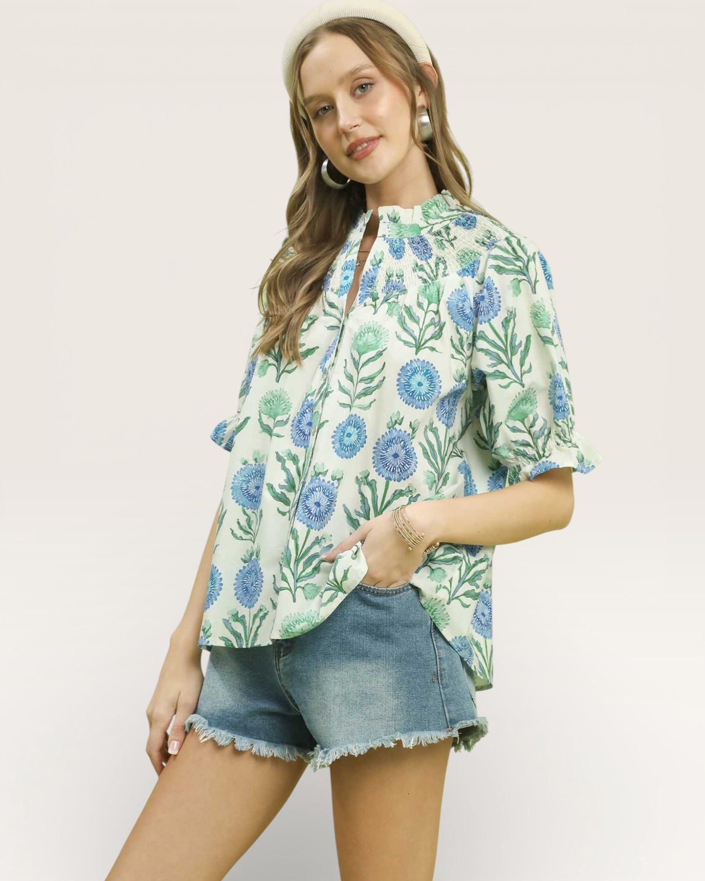 Woman wearing a floral blouse and denim shorts on a plain background