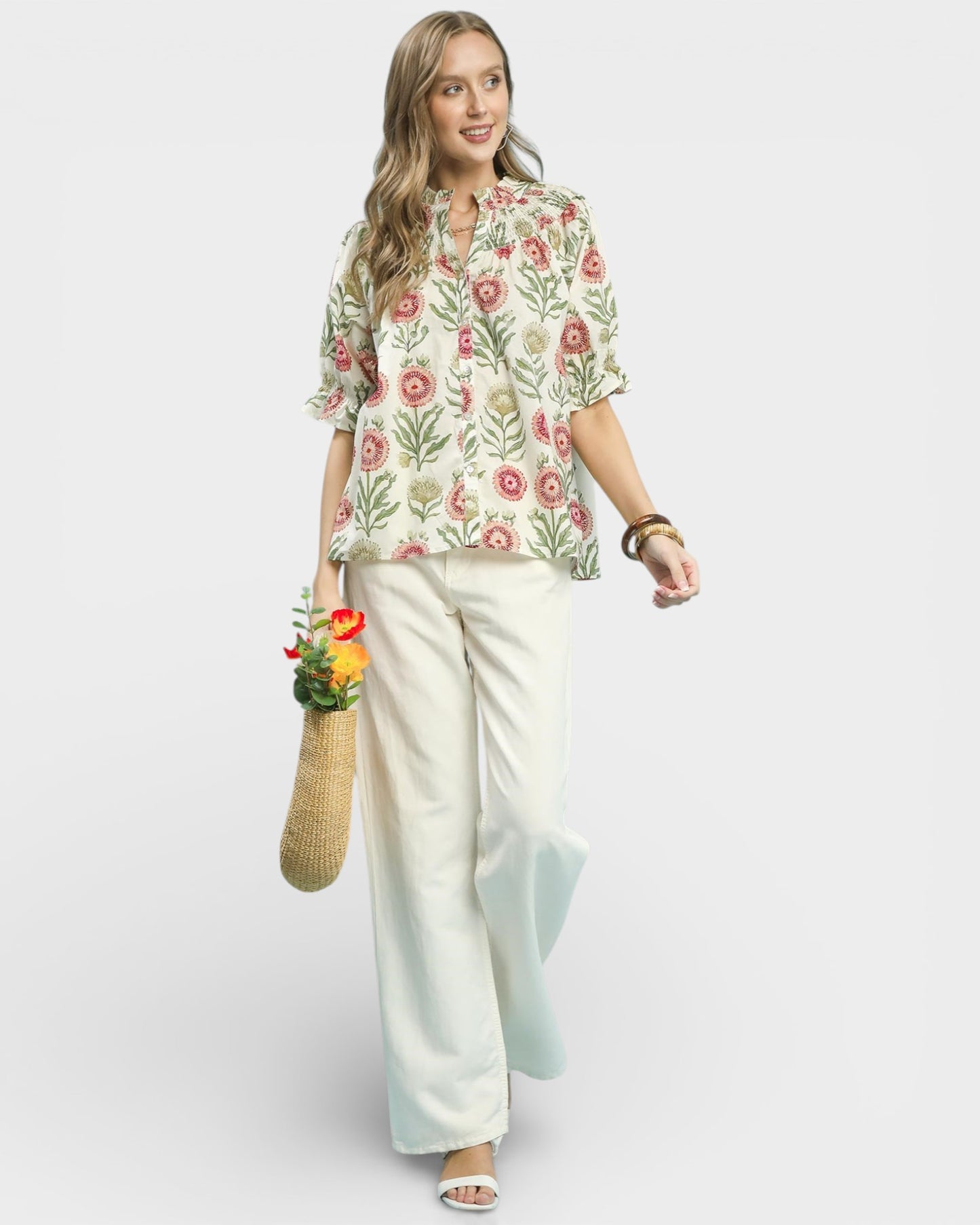Woman wearing a floral blouse and white pants on a light gray background