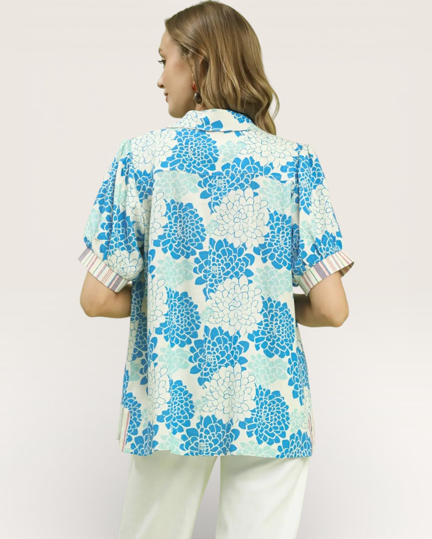 Woman wearing a floral patterned blouse with white pants on a plain background