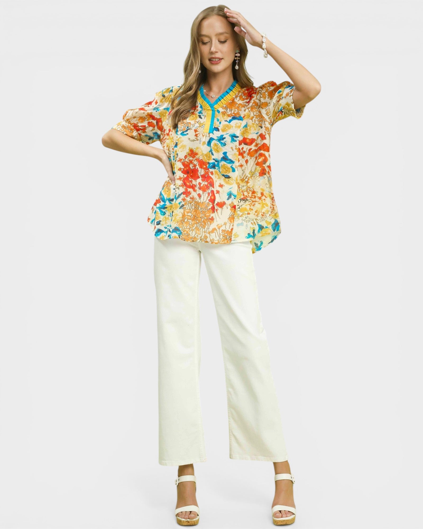 Woman wearing a colorful floral blouse and white pants on a plain background