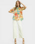 Woman wearing a colorful floral blouse and white pants on a plain background