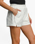 A close-up of a model wearing white textured shorts with a side slit and side pocket, paired with a black ribbed top against a plain white background.