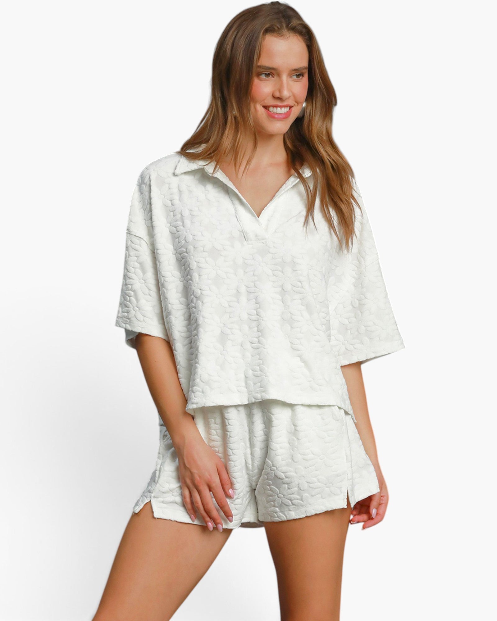 A woman modeling a matching two-piece lounge set in a textured off-white fabric, featuring a short-sleeve collared top and coordinating shorts, set against a plain white studio background.