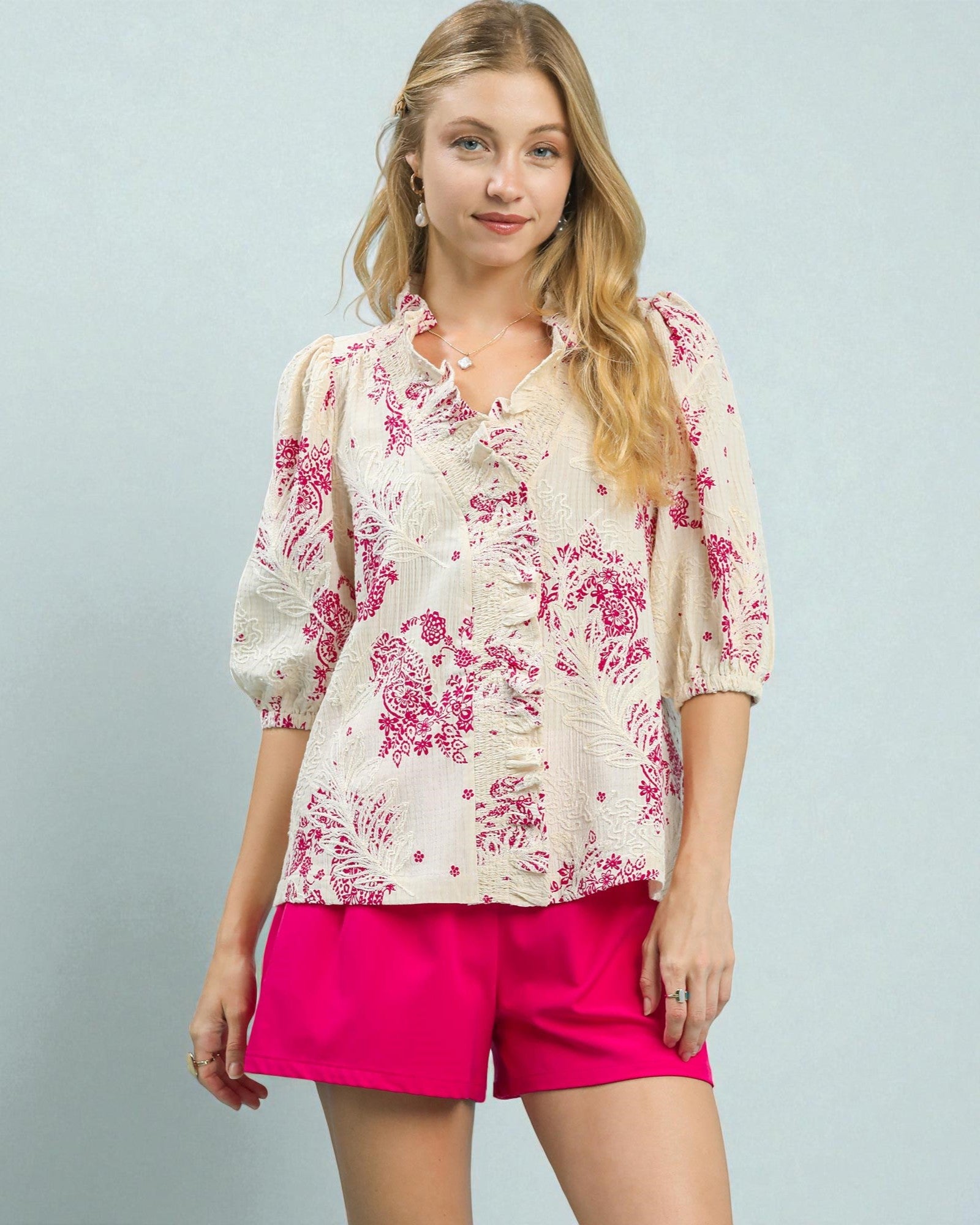 Woman wearing a floral blouse and pink shorts against a light gray background