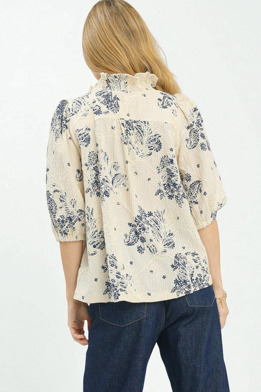 Woman wearing a cream floral blouse with blue pants on a white background