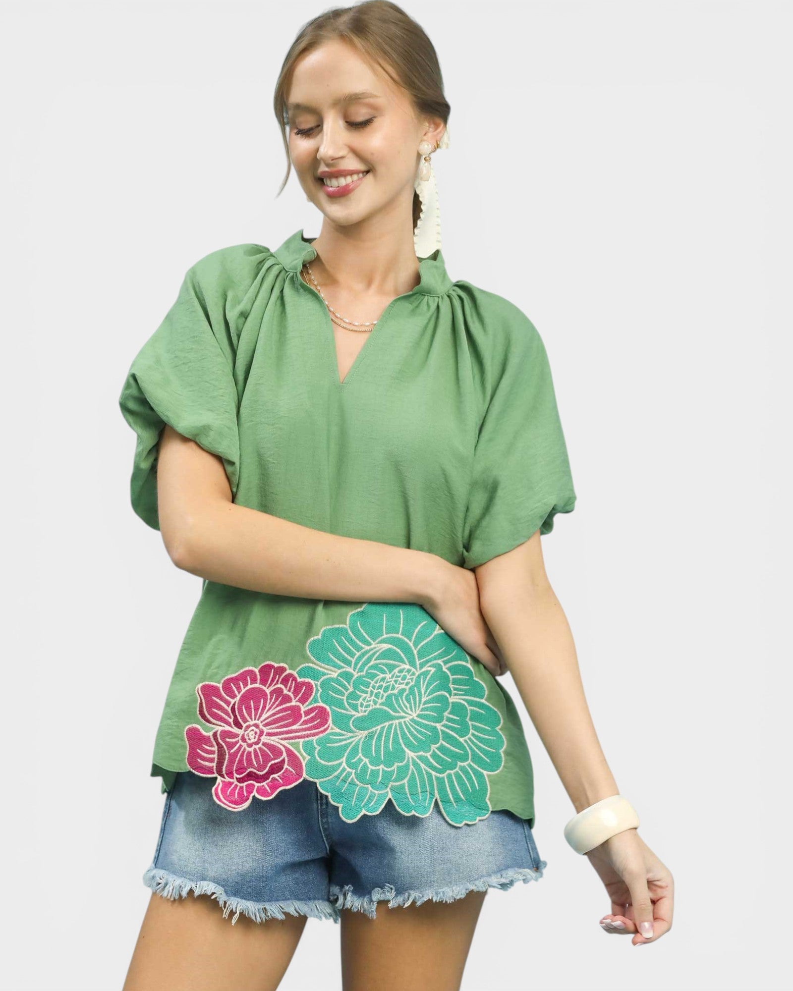 Woman wearing a green top with floral designs on a plain background