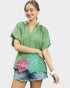 Woman wearing a green top with floral designs on a plain background